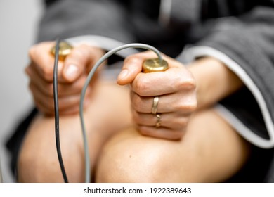Female patient takes hold of the brass handpieces of bioenergetic testing device in medical clinic. Health and wellness concept. Close up.