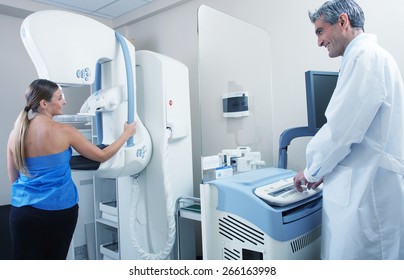 Female Patient Undergoing Scan At Mammography Machine With Male Doctor Supervisor. Happy Hospital Scene.