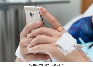 Female Patient Using Mobile Phone In Hospital Bed