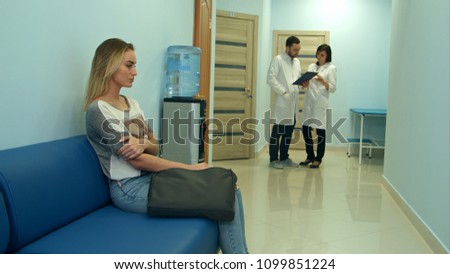 Female patient waiting in hospital hall while two doctors consulting