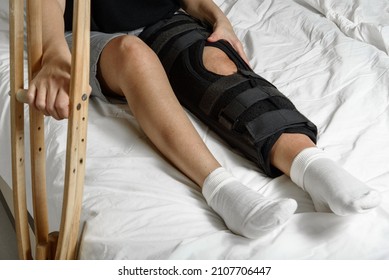 Female patient wearing orthosis sitting on bed holding crutches after surgery on broken leg. Rehabilitation of injured woman at home. Selective focus