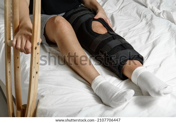 Female patient wearing orthosis sitting\
on bed holding crutches after surgery on broken leg. Rehabilitation\
of injured woman at home. Selective\
focus
