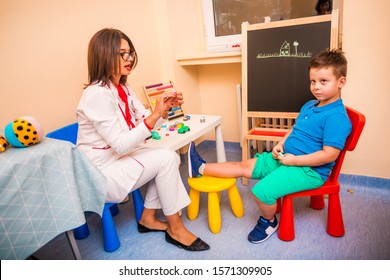 Female Pediatrician checking reflexes of young cute boy while he is sitting on the chair. - Shutterstock ID 1571309905