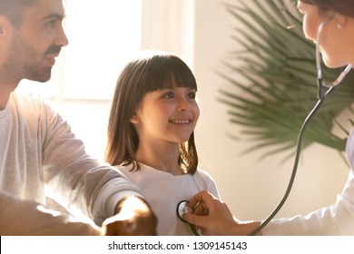 Female Pediatrician Holding Stethoscope Examining Happy Child Girl Visiting Doctor With Father, Nurse Checking Heart Lungs Of Kid Doing Pediatric Checkup In Hospital, Children Medical Insurance Care