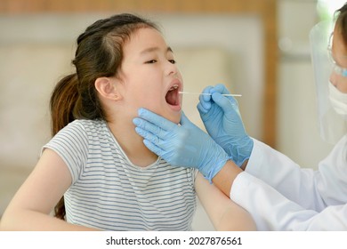 Female Pediatrician Using A Swab To Take A Sample From A Patient's Throat.Medical Worker Taking Mucus Specimen From Potentially Infected Asian Child. Covid-19 Nasal Swab Test.