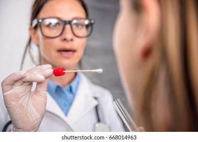 Female pediatrician using a swab to take a sample from a patient's throat - Powered by Shutterstock