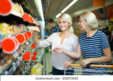 Female pensioner and her daughter choosing chilled sausages in shop