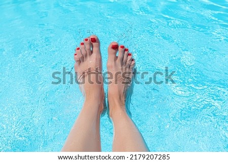 Female with perfect red pedicure over a pool with water splash. Vacation pericure. Female with bare feet over blue swimming pool water