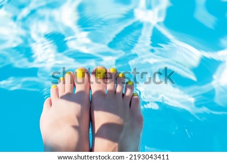 Female with perfect yellow pedicure over a pool with water splash. Vacation pericure. Female bare feet with beautifull yellow pedicure in a blue swimming pool water
