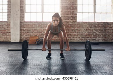 Female Performing Deadlift Exercise With Weight Bar. Confident Young Woman Doing Weight Lifting Workout At Gym.