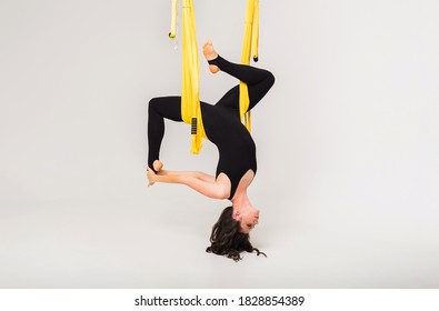 female performs an inverted anti-gravity yoga pose in a yellow hammock on a white isolated background with a copy of the space. Side view