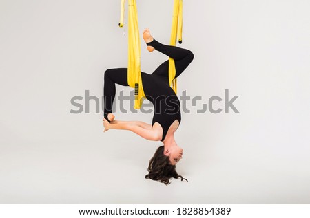 female performs an inverted anti-gravity yoga pose in a yellow hammock on a white isolated background with a copy of the space. Side view