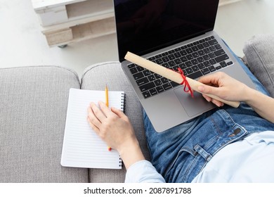 Female person with a diploma scroll sitting on the couch at home, holding a laptop on her lap. Concept for online student, distance learning, online university, secondary education, modern development - Shutterstock ID 2087891788