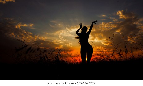 Female person doing yoga in steppe, silhouette in sunset background. Concept of dancing meditation and relaxing on nature.