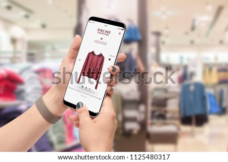 Female person shopping online with smartphone, clothing store in background