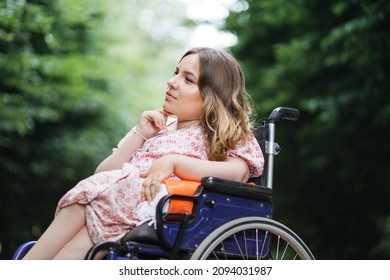 Female person with spinal muscular atrophy spending time outdoors alone with her thoughts. Young woman who using wheelchair sitting among green summer park and looking aside. - Shutterstock ID 2094031987