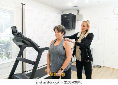 A Female Personal Trainer Helping A Senior Client Exercise, Train, And Build Muscle Using Small Hand Weights In A Gym.