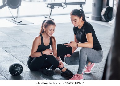 Female Personal Trainer With Notepad Showing Young Woman Results.