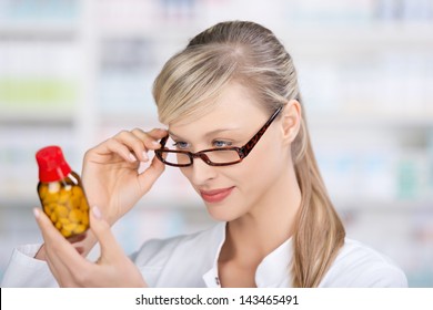 Female Pharmacist Attentively Reading The Medicine Label Of A Bottle Of Pills