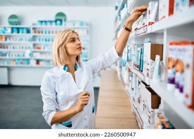 Female pharmacist checking medicine supplies on shelves while working in a pharmacy. - Powered by Shutterstock