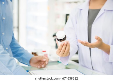 Female pharmacist holding medicine bottle giving advice to customer in chemist shop or pharmacy