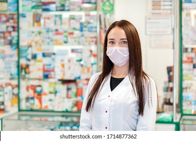 A female pharmacist in a medical mask poses against the background of a pharmacy window in a blur. Concept of virus protection and pharmacy business