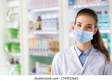 A Female Pharmacist In A Medical Mask Poses Against The Background Of A Pharmacy Window