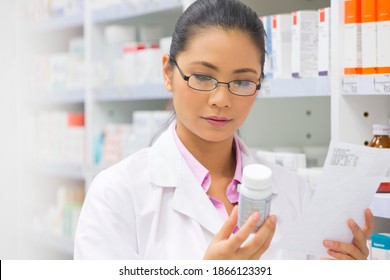 Female pharmacist with a prescription reading the label on a medication pot next to a pharmacy shelf.