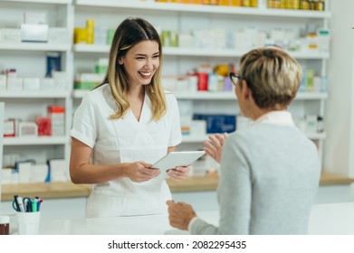 Female pharmacist selling medications at drugstore to a senior woman customer while using a tablet - Powered by Shutterstock