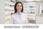 Female pharmacist standing near racks with cosmetics. Woman druggist conducting audit of new supply of medicine. Woman pharmacist holding tablet. Female druggist wearing white gown in drugstore.