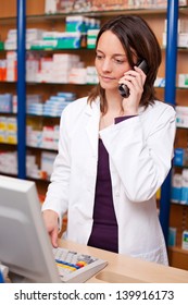 Female Pharmacist Using Cordless Phone At Pharmacy Desk