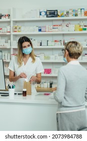 Female Pharmacist Wearing Protective Mask And Serving A Customer Patient In A Pharmacy And Packing Drugs In A Paper Bag