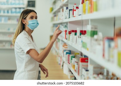 Female Pharmacist Wearing Protective Mask And Choosing Medicine In Pharmacy Store