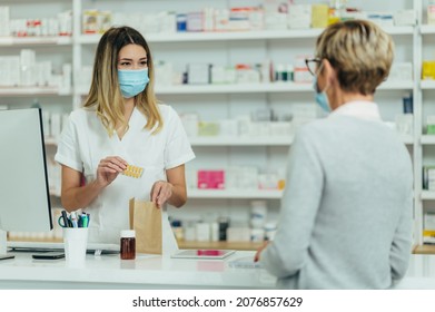 Female Pharmacist Wearing Protective Mask And Serving A Customer Patient In A Pharmacy And Packing Drugs In A Paper Bag