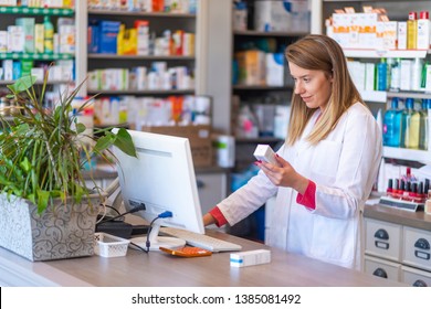 Female pharmacist working in chemist shop or pharmacy. Pharmacist using the computer at the pharmacy. Portrait of young female pharmacist holding medication while using computer at pharmacy counter 