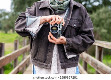 Female photographer adjusting settings on her vintage camera while standing on a wooden bridge in a natural outdoor setting, capturing the essence of classic photography - Powered by Shutterstock - Get 15% off with code: PIKWIZARD15