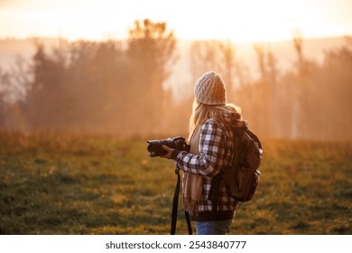 Female photographer with camera capturing the beauty of sunset in autumn nature. Hipster woman enjoying walk outdoors - Powered by Shutterstock