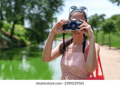 Female photographer in pink mesh top using a camera outdoors with greenery and lake in background. - Powered by Shutterstock