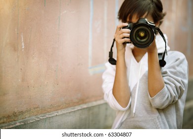 female photographer with professional SLR camera, natural light, selective focus on nearest part of lens with blend