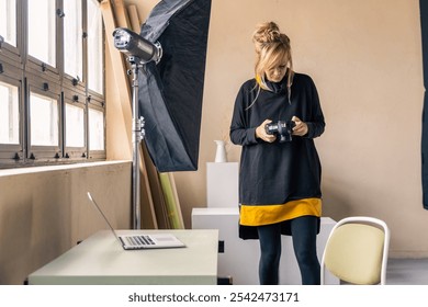 Female photographer reviewing captured images on her digital camera in a studio setting, surrounded by equipment - Powered by Shutterstock