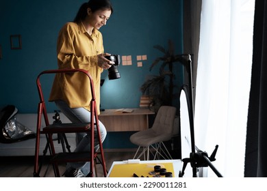 Female photographer setting up camera in home studio. Modern blogger. Content creator. Woman shooting photos. Copy space - Powered by Shutterstock