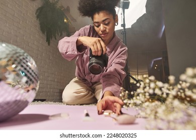 Female photographer take photo of disco ball, jade roller, face brush, ice and blossom tree branch on digital camera at home studio. Content for photostocks, commerce, social networks and advertising