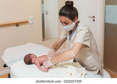 Female Physical Therapist Wearing A Face Mask While Working With A Newborn Baby In A Medical Center.