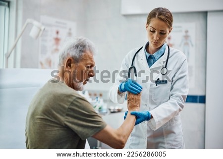 Female physical therapists checking senior patient's hand at medical clinic. 