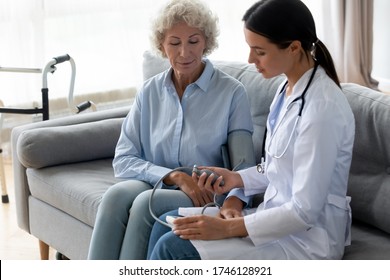 Female physician caring about old woman manually takes blood pressure using sphygmomanometer seated on sofa, checks arterial pressure, hypertension hypotension cardiovascular diseases control concept