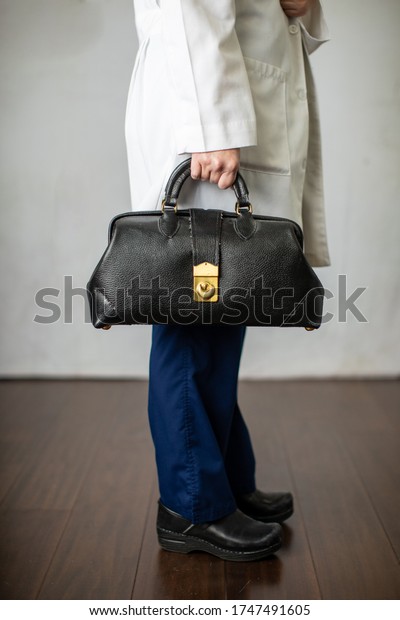 Female physician holding a\
black leather doctor\'s bag heading to the office to practice\
medicine