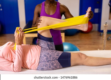 Female physiotherapist assisting woman to exercise with resistance band in sports center. Sports Rehab Centre with physiotherapists and patients working together towards healing - Powered by Shutterstock