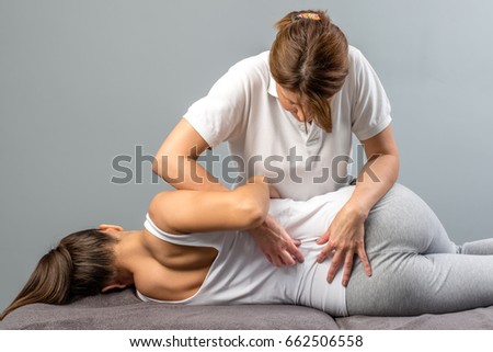 Female physiotherapist doing manipulative spine treatment on young patient.