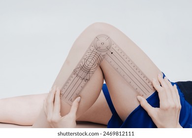 Female physiotherapist examining knee angle of patient with goniometer. on the background of a white wall in the hospital - Powered by Shutterstock