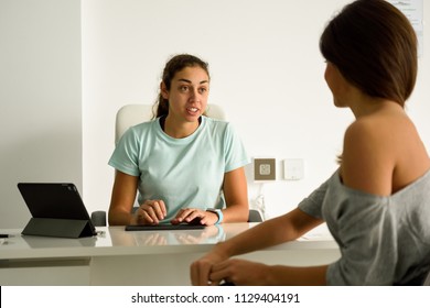 Female physiotherapist explaining diagnosis to her patient. Brunette woman having consultation with girl in medical office. - Shutterstock ID 1129404191